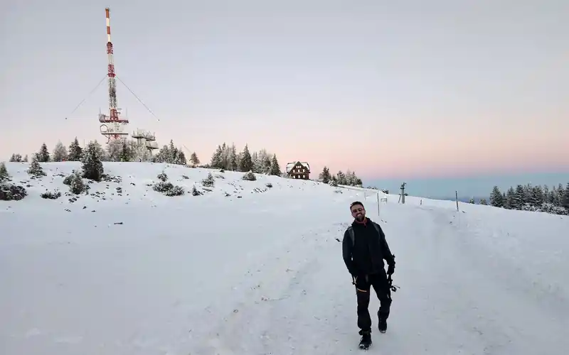 Ingo walking on a snowy mountain path at dawn, a transmitter tower behind him